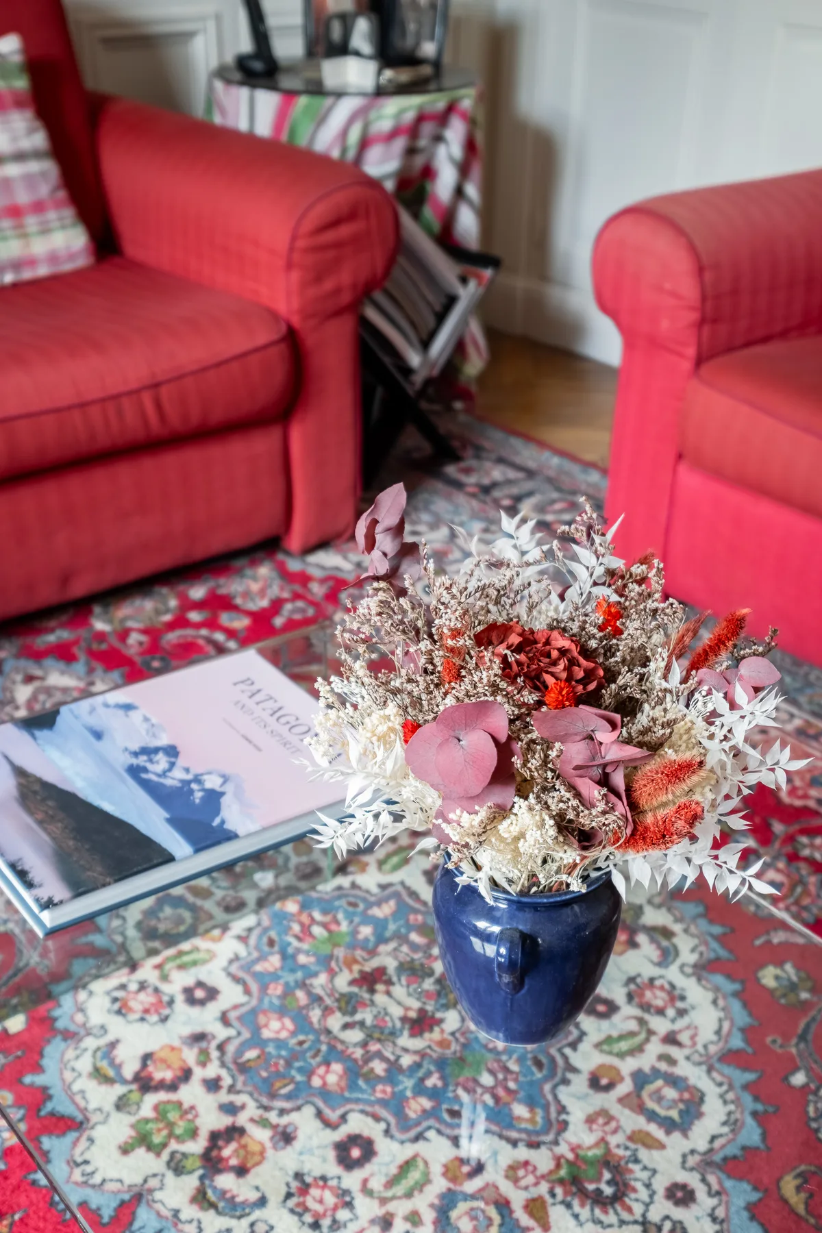 Una zona de estar con sillones rojos junto a una alfombra estampada y flores.