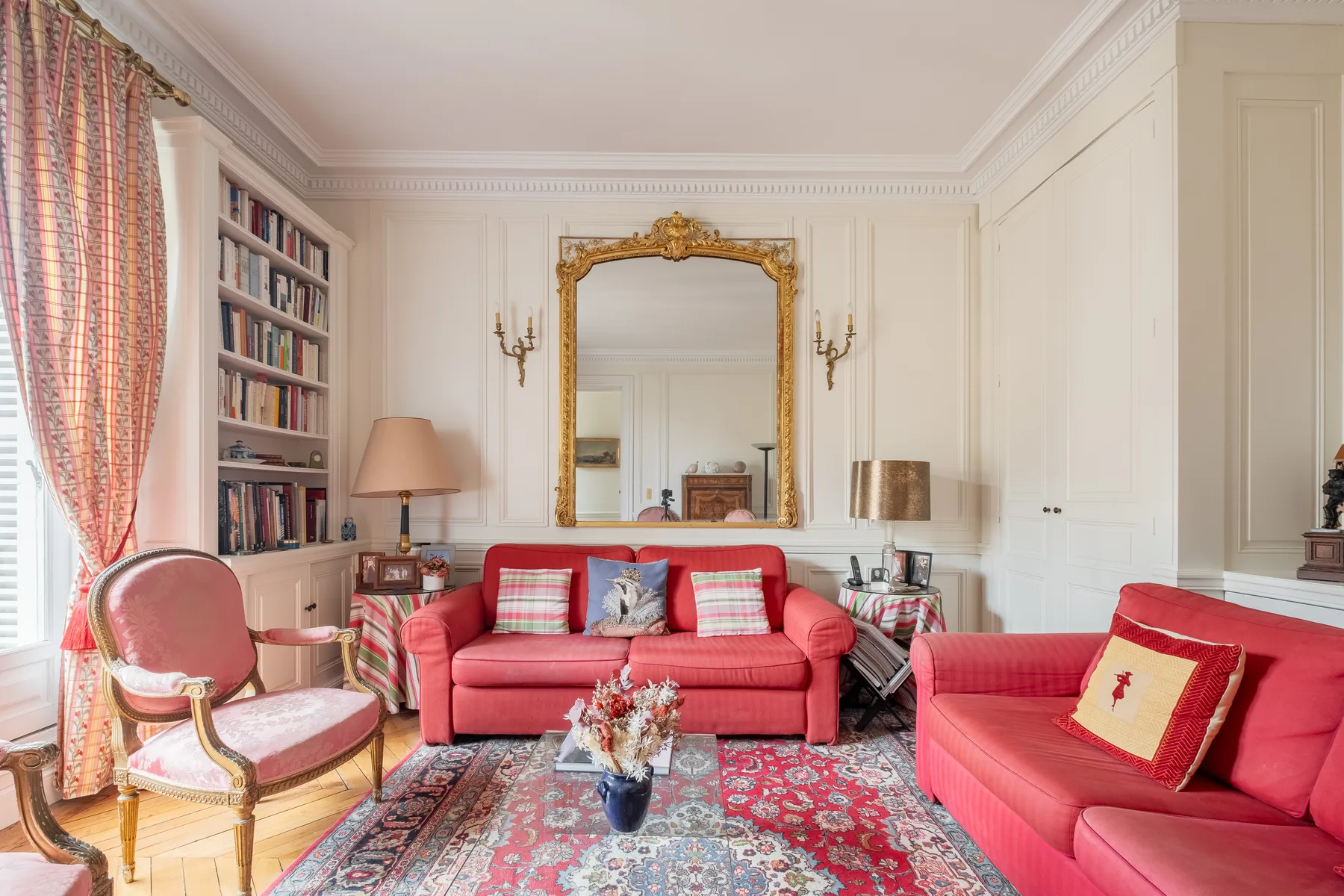 Una sala de estar con asientos rojos, estanterías y un gran espejo ornamentado.