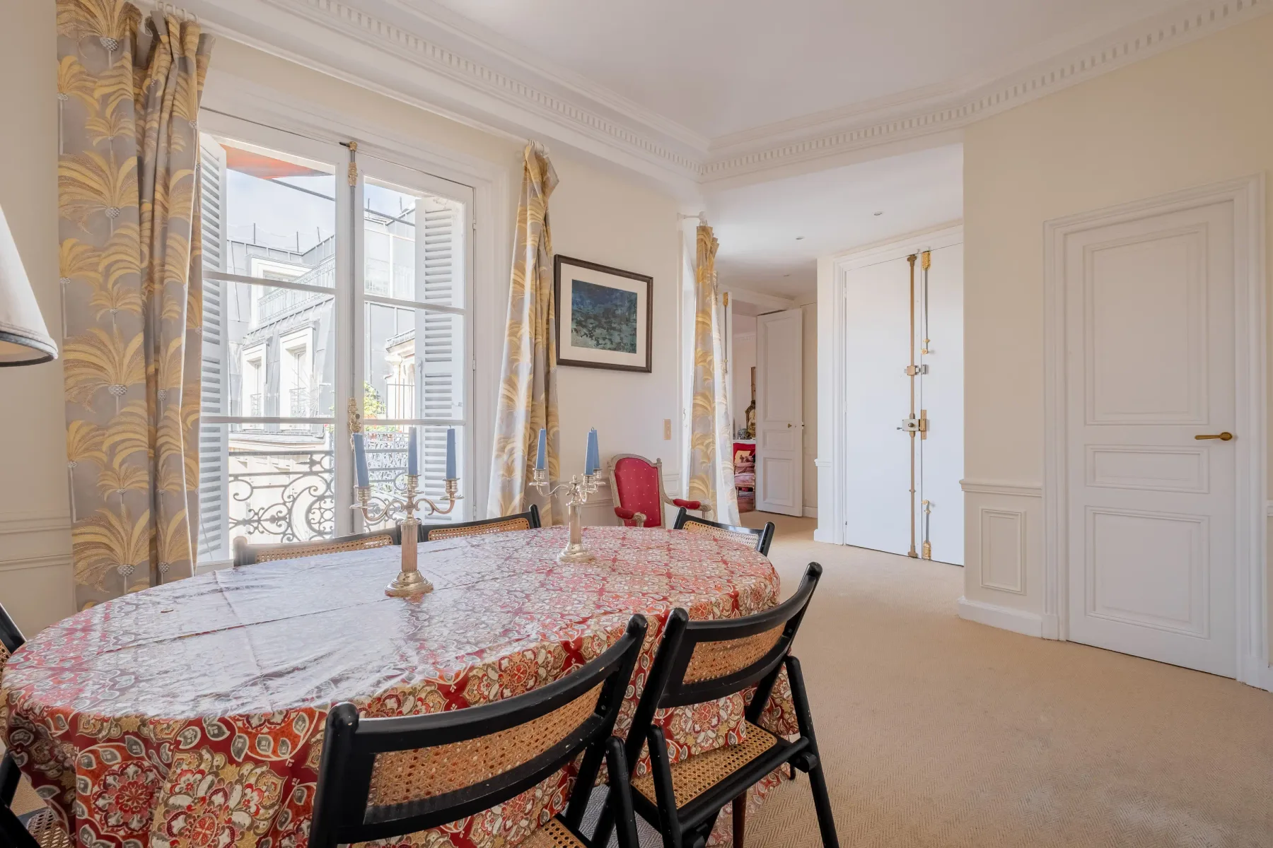 Un comedor luminoso con un mantel estampado y ventanas altas.