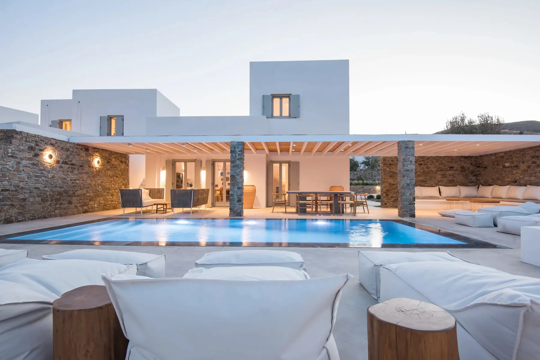 A modern villa opens onto a swimming pool and outdoor seating area.