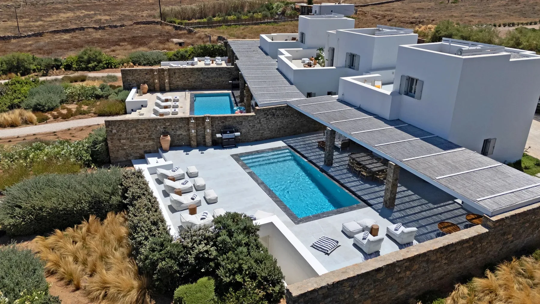 A white villa overlooks a pool and outdoor seating area.