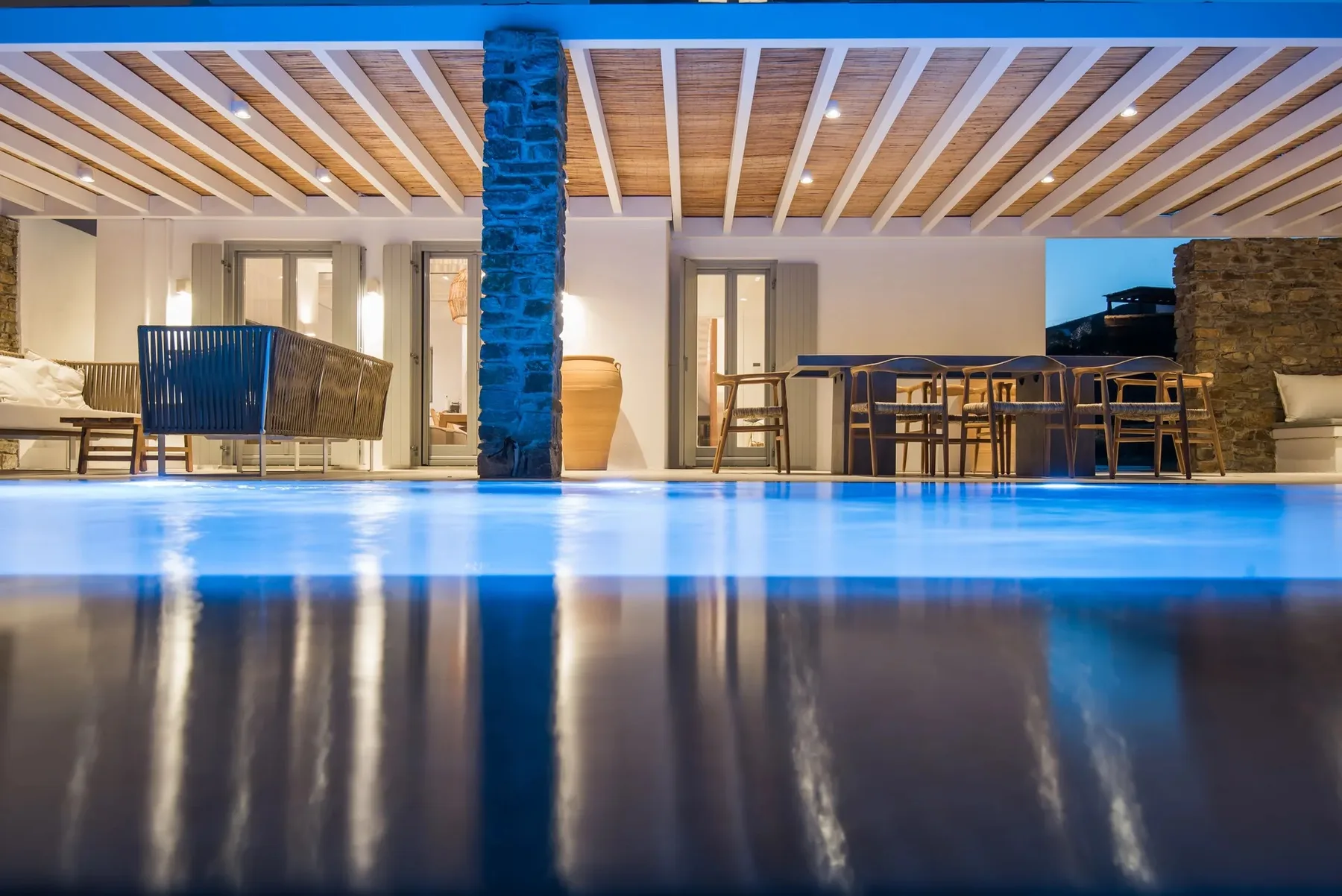 A poolside patio with a dining area beneath a timber-beamed roof.