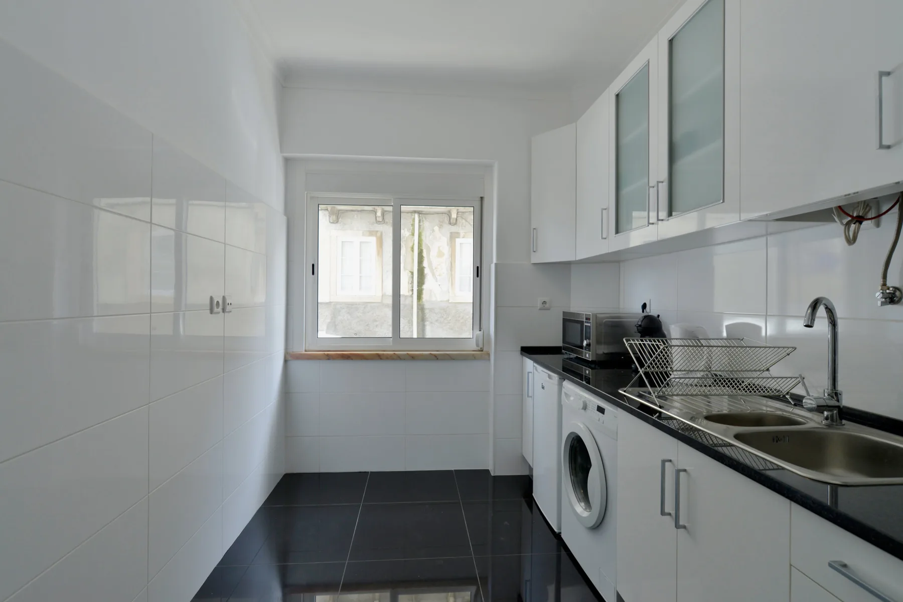 A bright kitchen with white cabinets, a dark countertop, and a window.