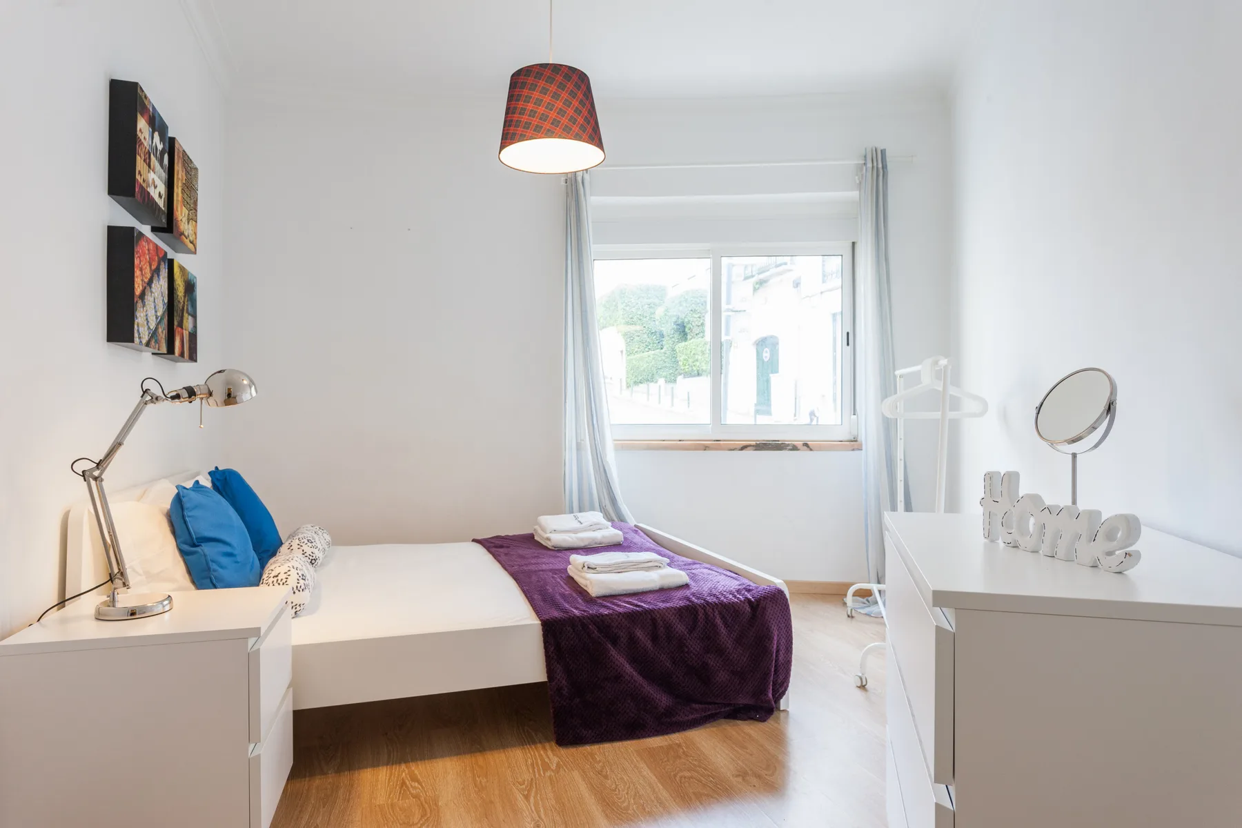 A bright bedroom with a bed, bedside lamp, and window.