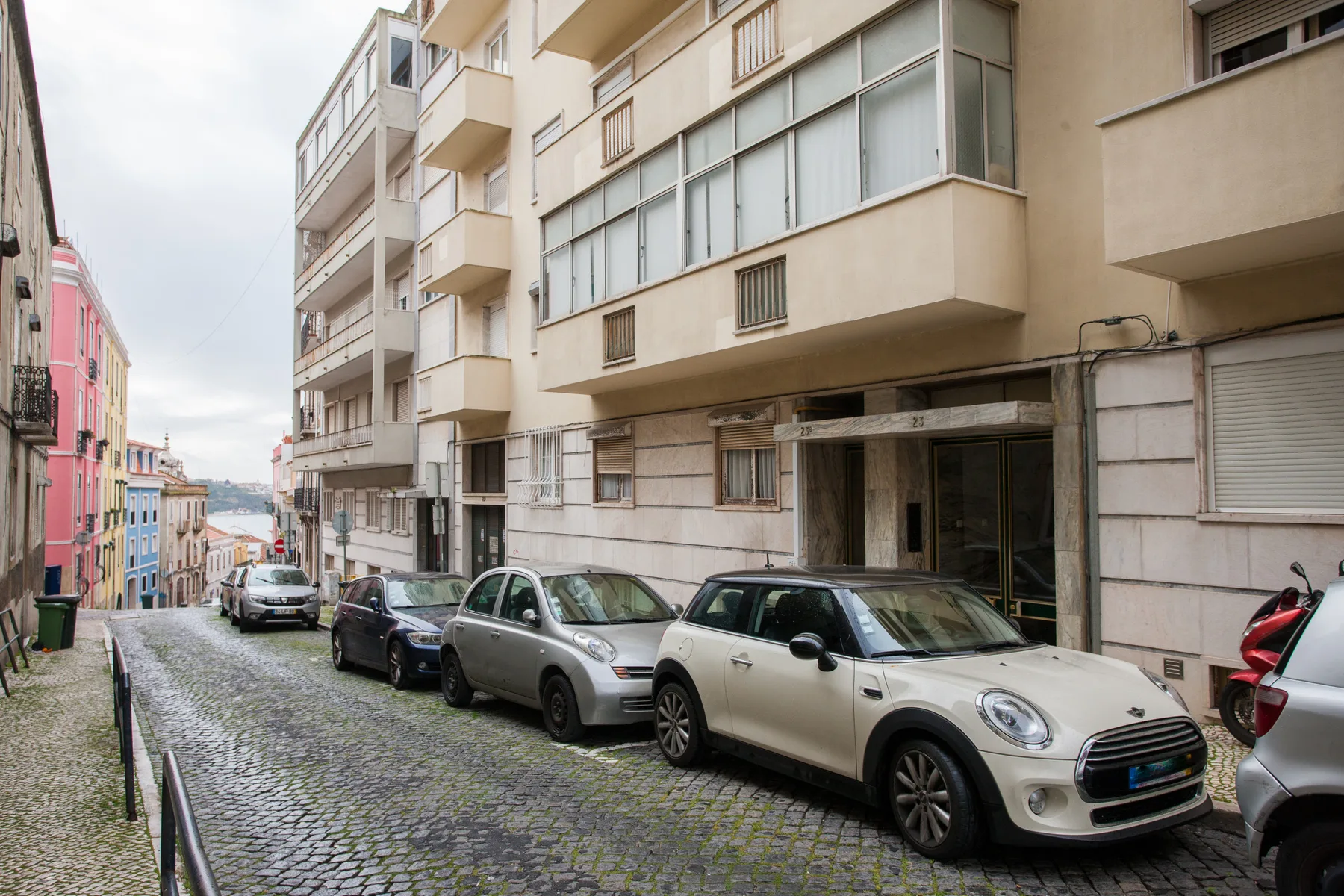 A cobblestone street lined with apartment buildings and parked cars.