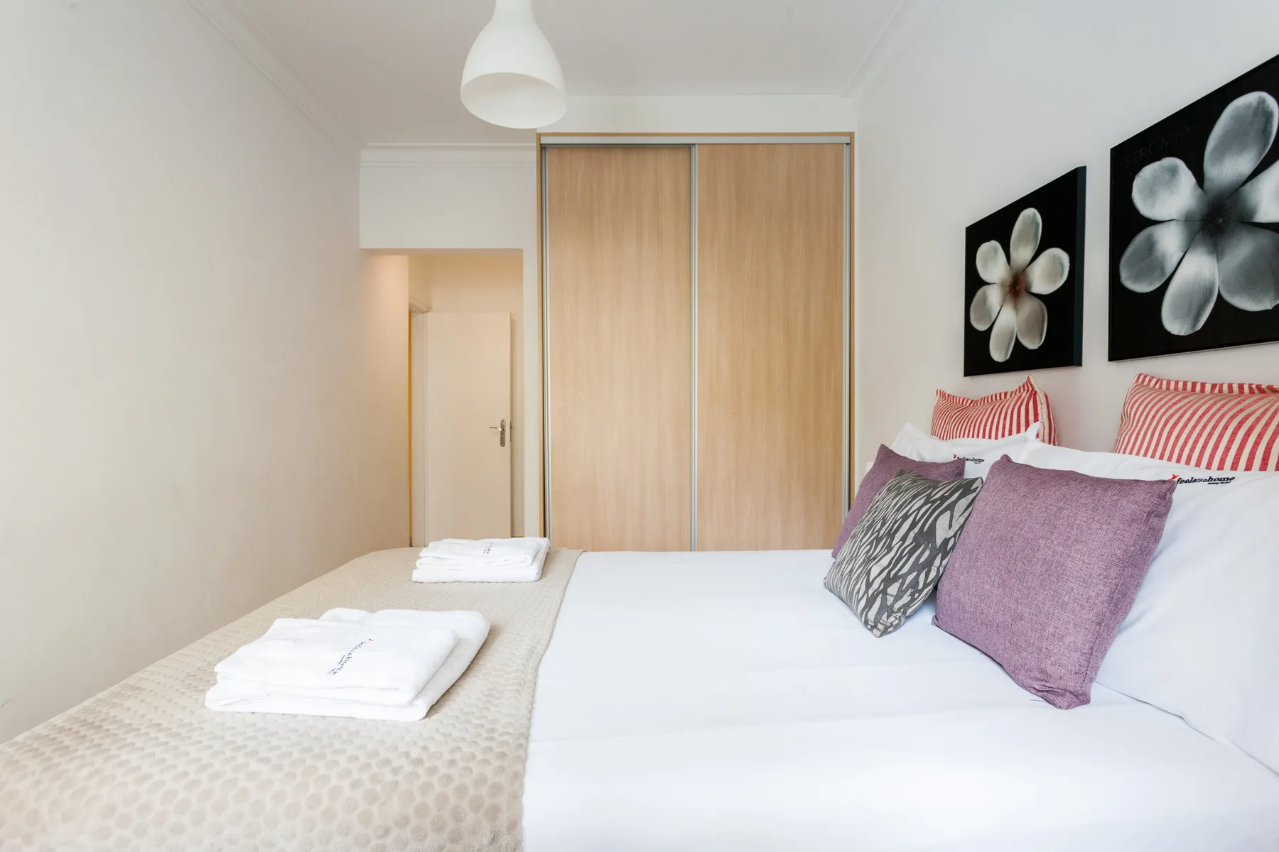 A bedroom with a neatly made bed and floral artwork above the pillows.