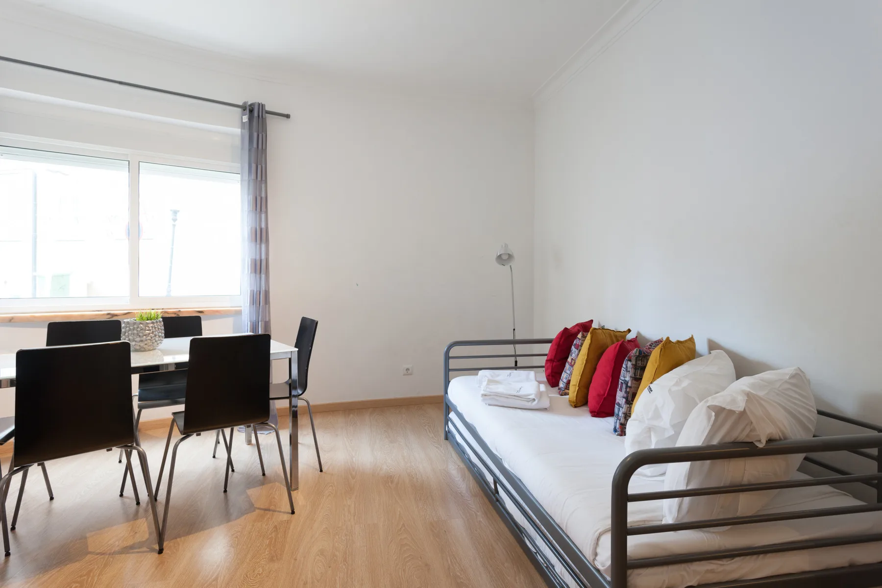 A bright living area combines a metal-frame bed with a dining table by the window.