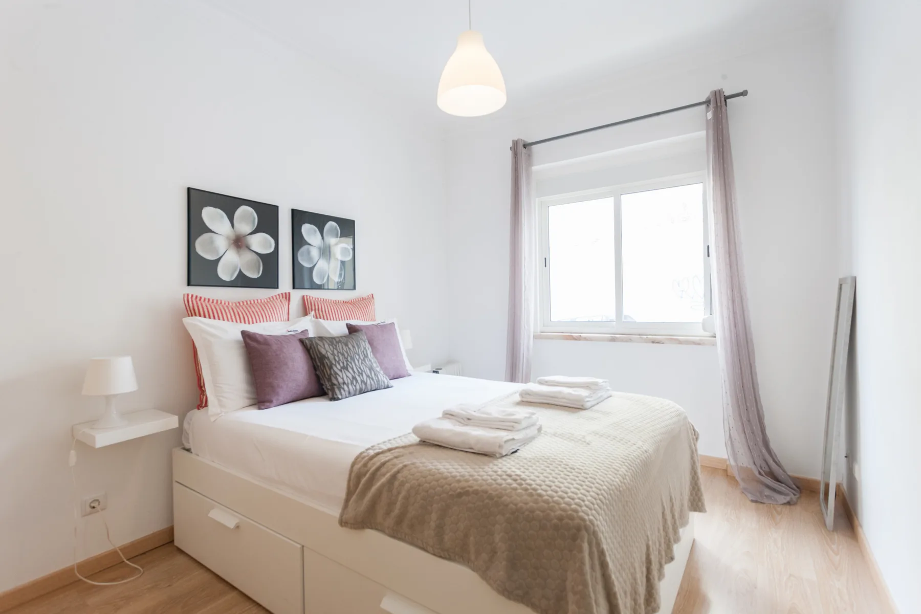 A bright bedroom with a bed beneath two floral wall prints.