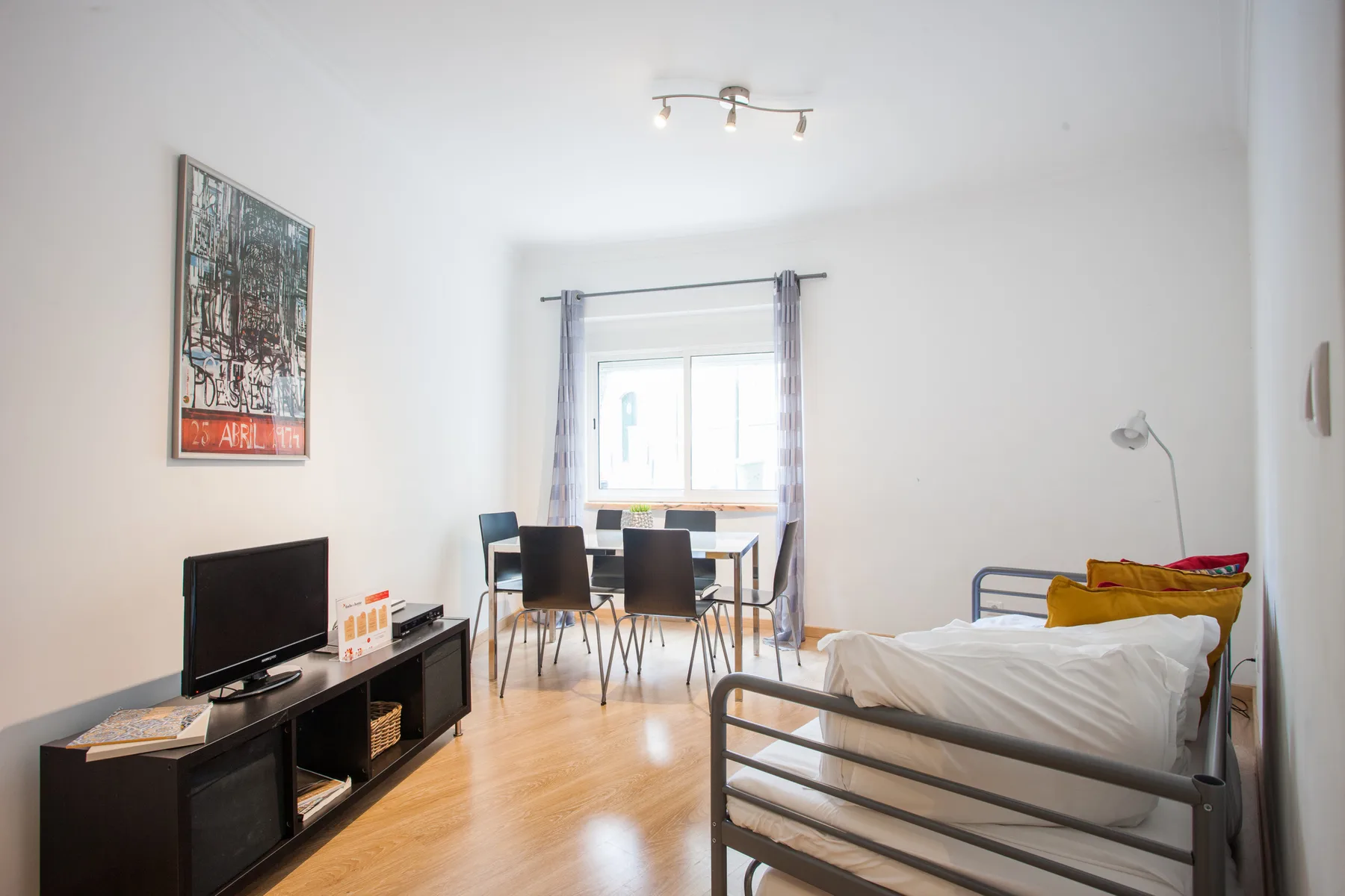 A bright bedroom with a bed, television, and dining table by the window.