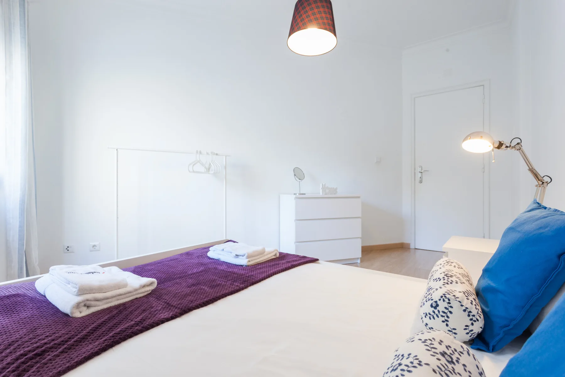 A bright bedroom with a neatly made bed and a dresser.