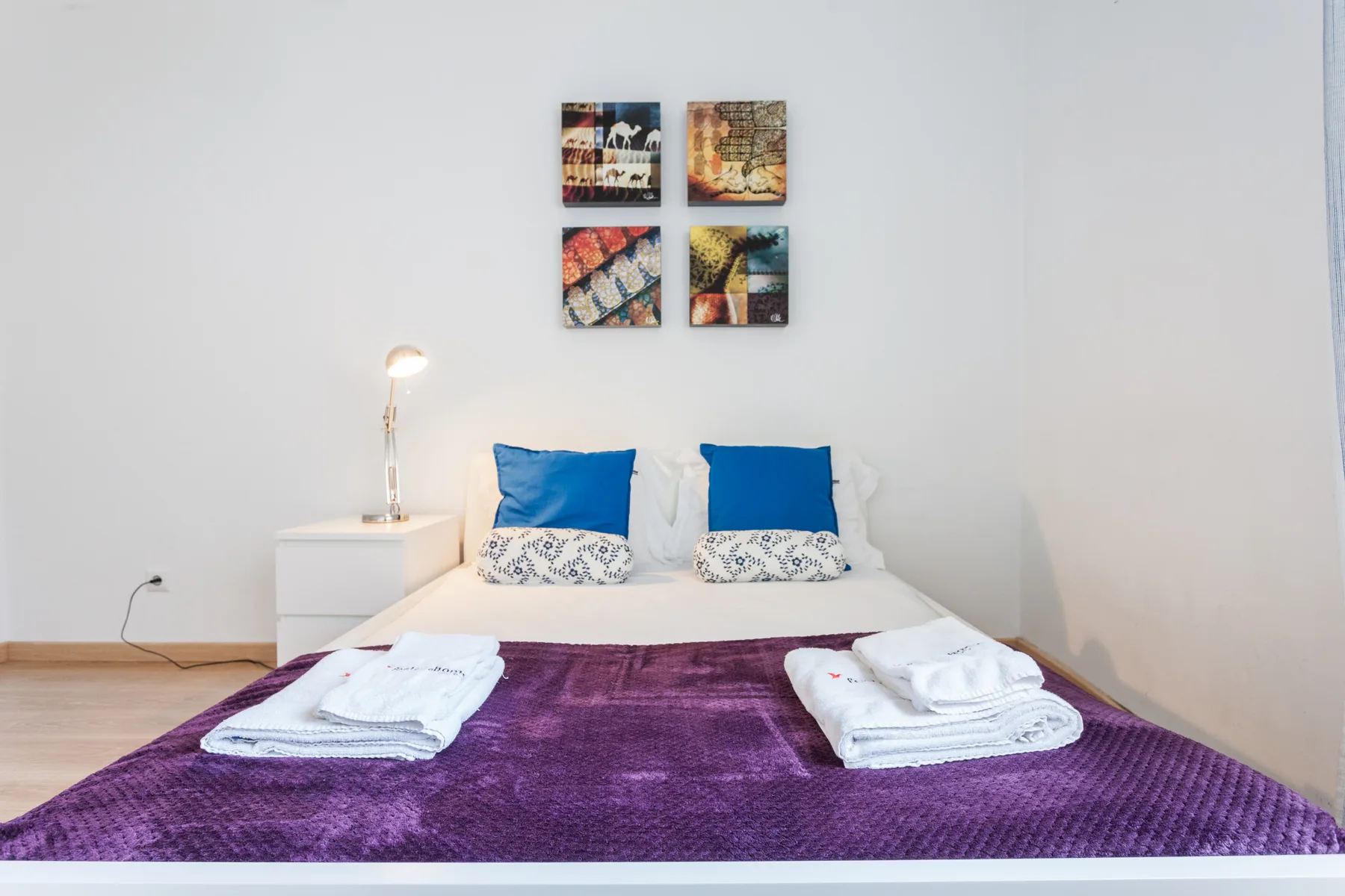 A bedroom with a bed, blue pillows, and folded towels on a purple cover.