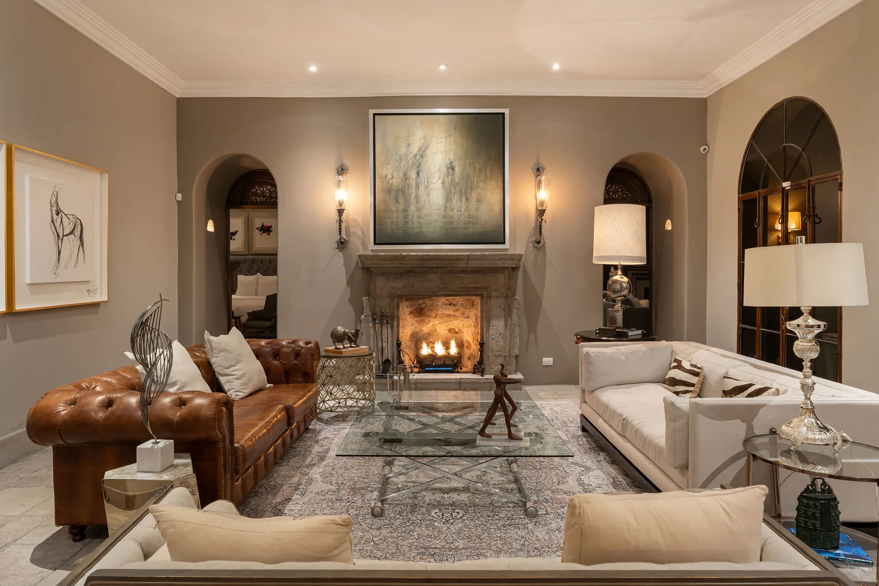 A living room with seating arranged around a fireplace and glass coffee table.