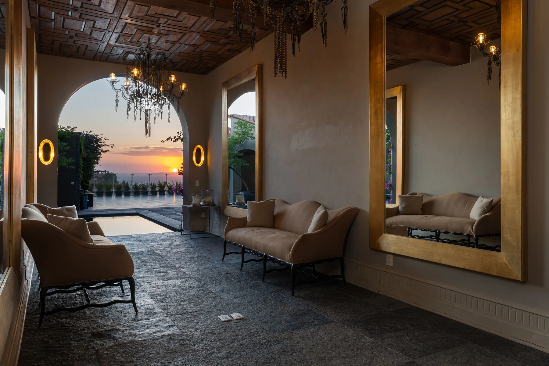 A lounge with cushioned seating, a large mirror, and an arched opening to a pool.