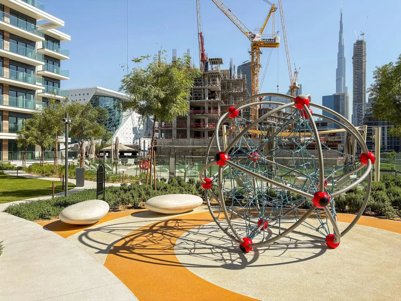 Una estructura para trepar está en un parque ajardinado al aire libre, con edificios de la ciudad al fondo.