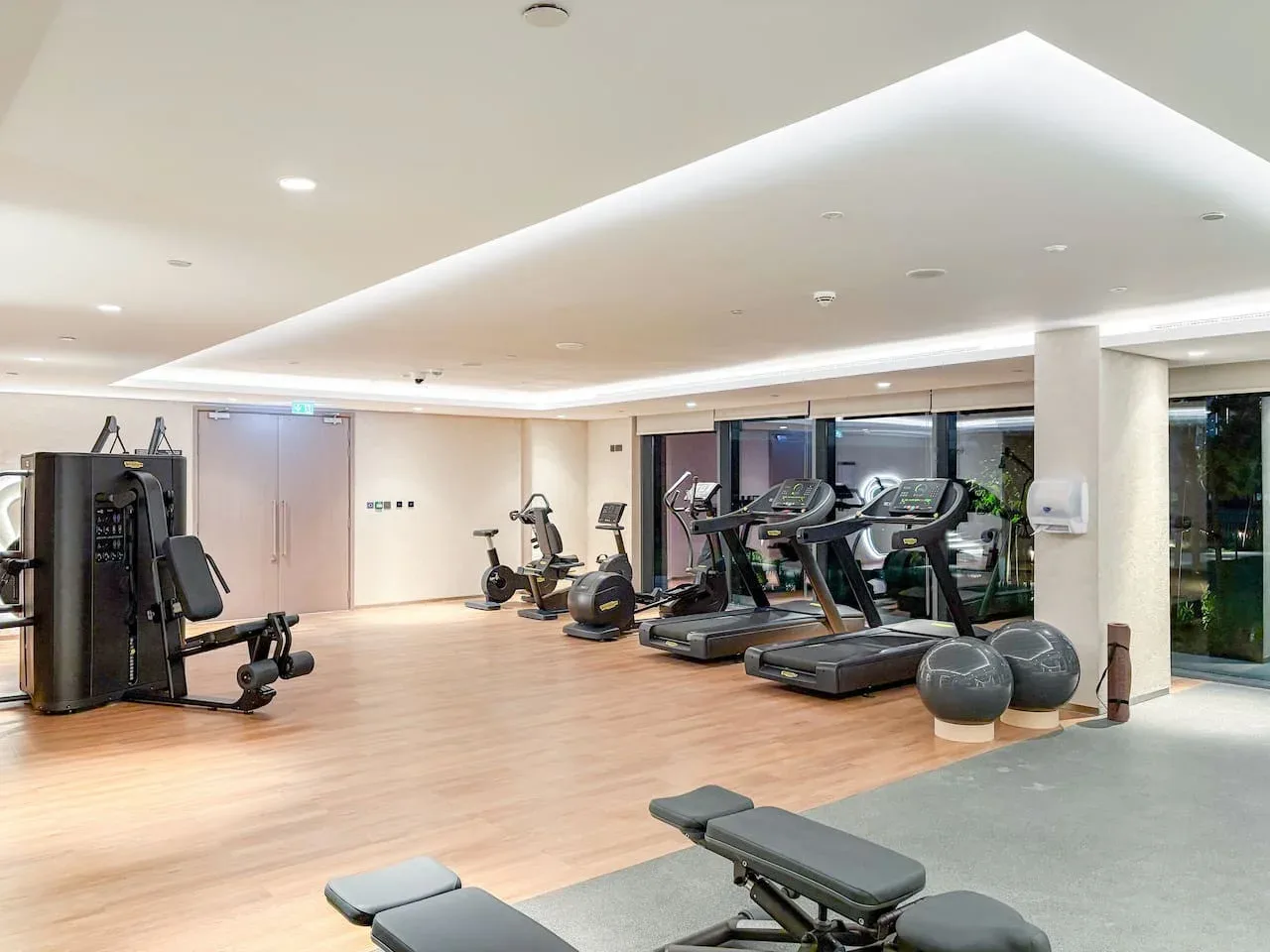 Un gimnasio luminoso con cintas de correr y equipos de musculación sobre un suelo de madera.