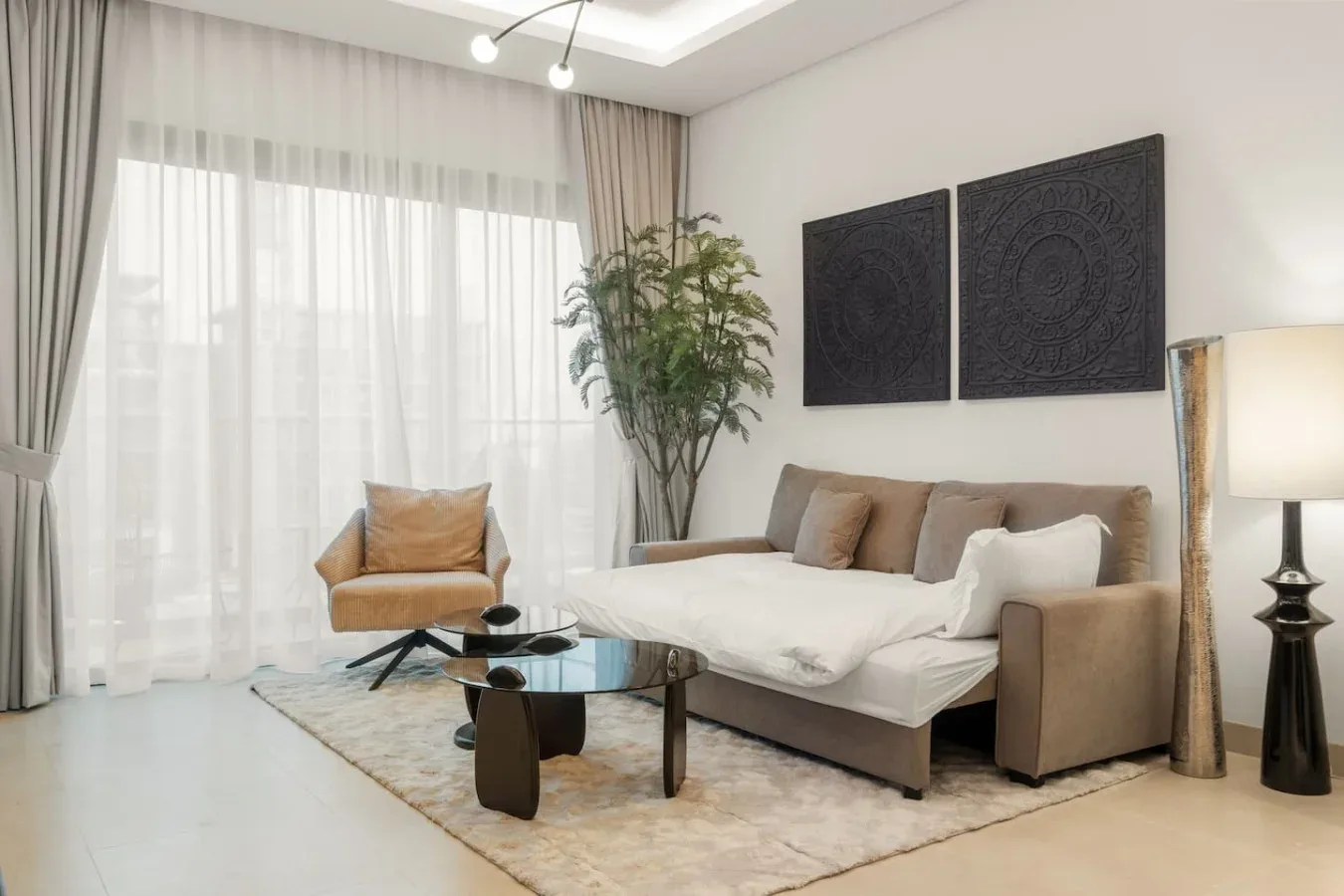 Una sala de estar con sofá, sillón, mesa de centro y una gran ventana con cortinas.