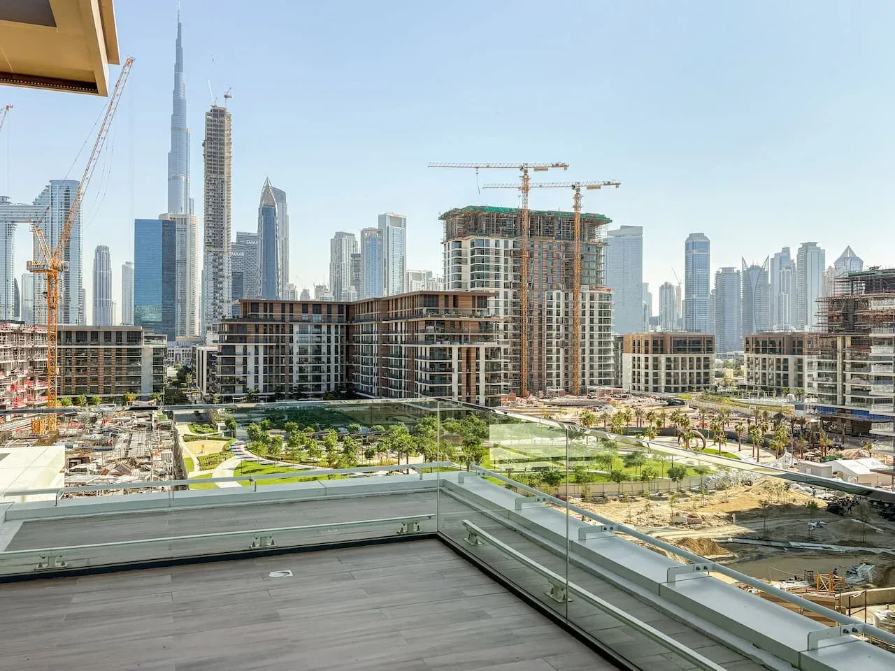 Un balcón da a zonas ajardinadas, obras y el horizonte de la ciudad.