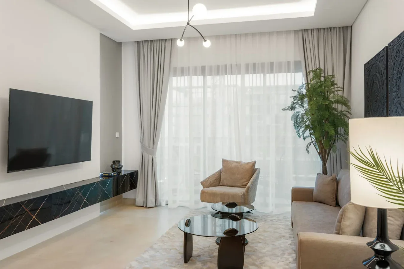 Una sala de estar con asientos, mesas de centro de vidrio y una gran ventana con cortinas.