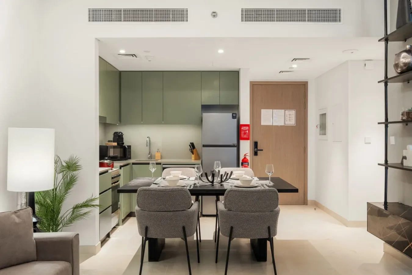 Una mesa de comedor con asientos está en una cocina luminosa con gabinetes verdes.