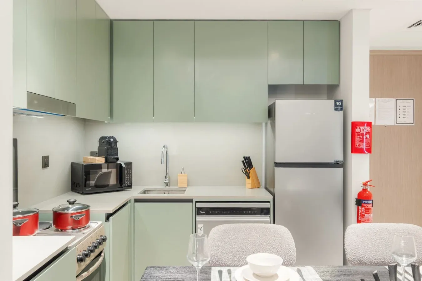 Una cocina moderna con gabinetes verde pálido, electrodomésticos de acero inoxidable y una mesa de comedor.