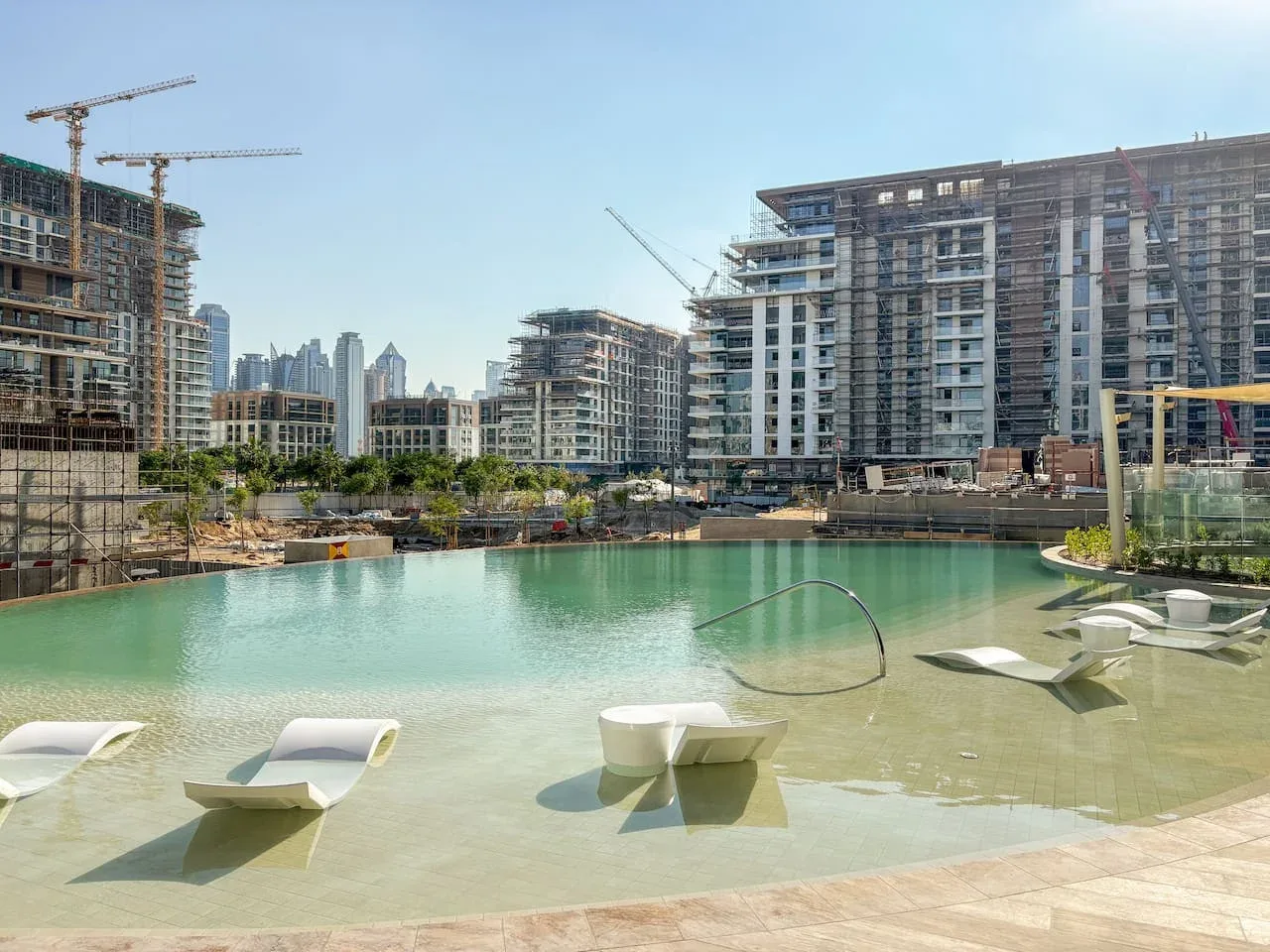 Una piscina exterior poco profunda se encuentra frente a edificios de apartamentos modernos en construcción.