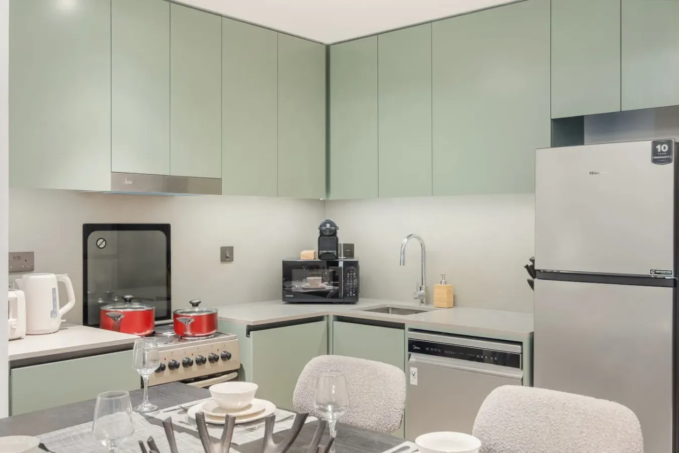Una cocina moderna con gabinetes claros, un refrigerador y una mesa de comedor en primer plano.