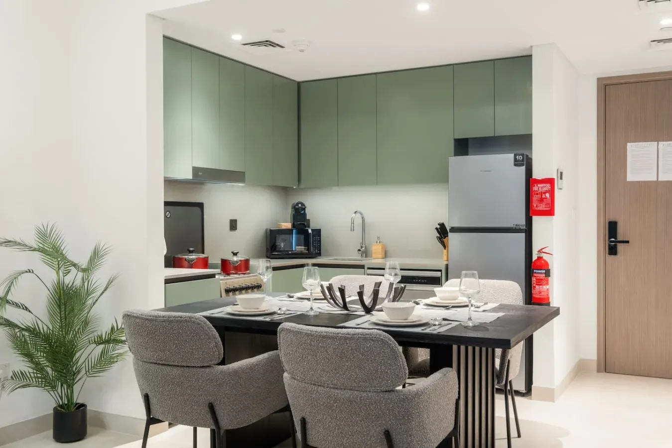 Comedor con la mesa puesta junto a una cocina con armarios verdes.