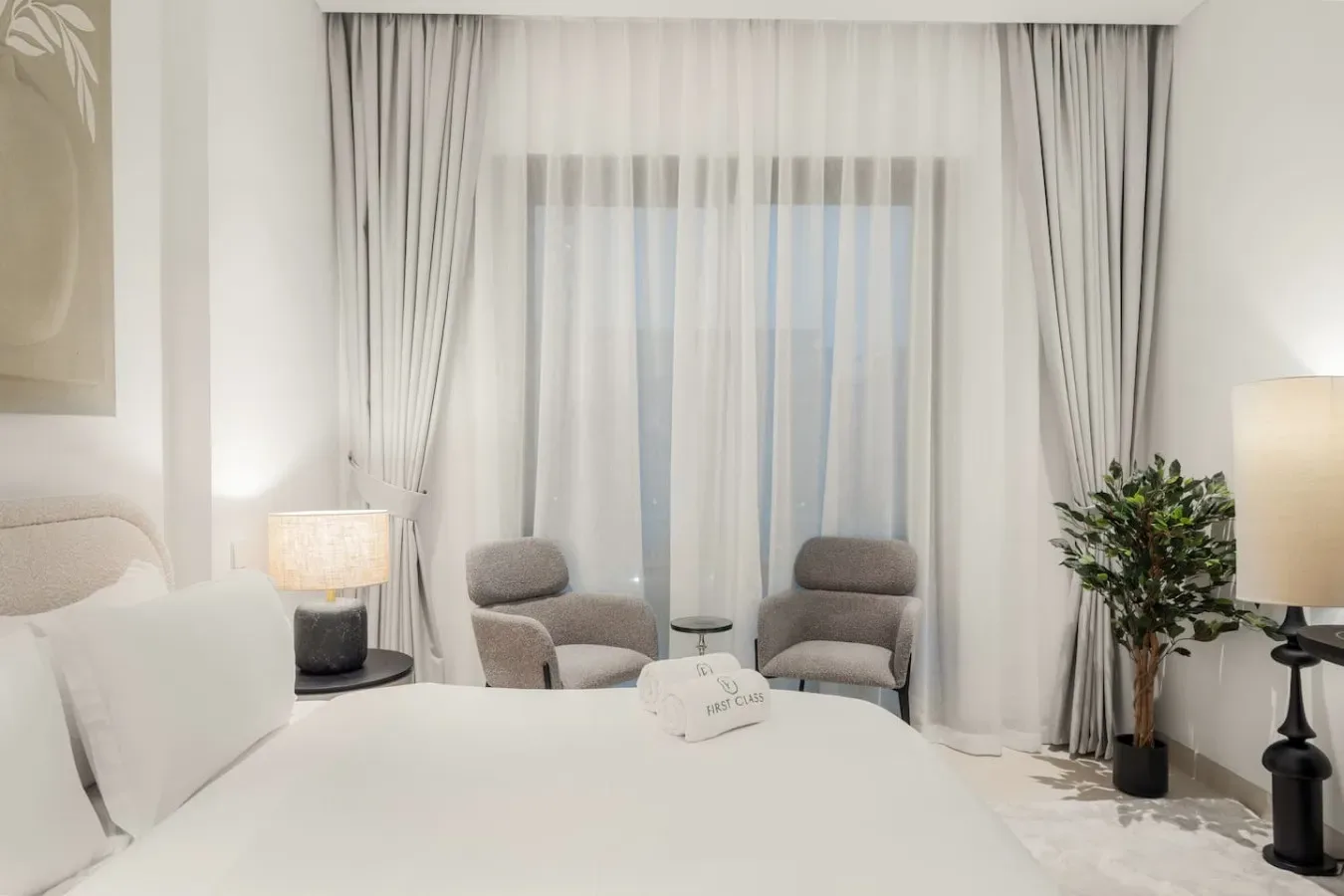 Un dormitorio con cama, asientos y cortinas que cubren una ventana grande.