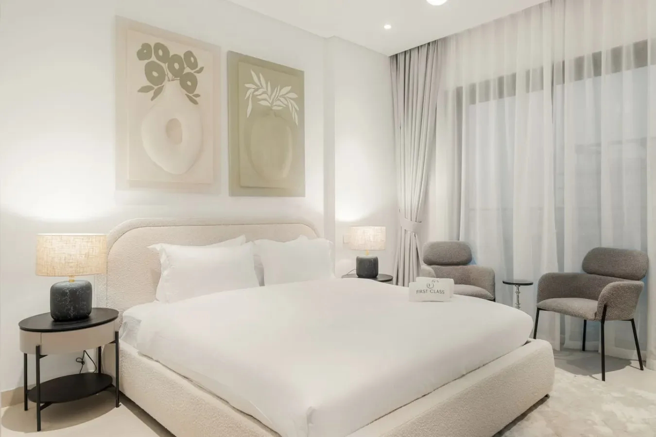 Un dormitorio luminoso con una cama grande, cuadros botánicos y ventanas con cortinas.