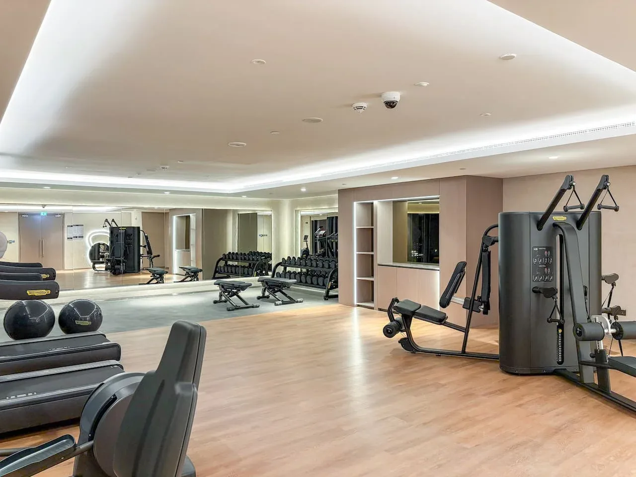 Un gimnasio amplio con máquinas de ejercicio, pesas y una pared con espejos.