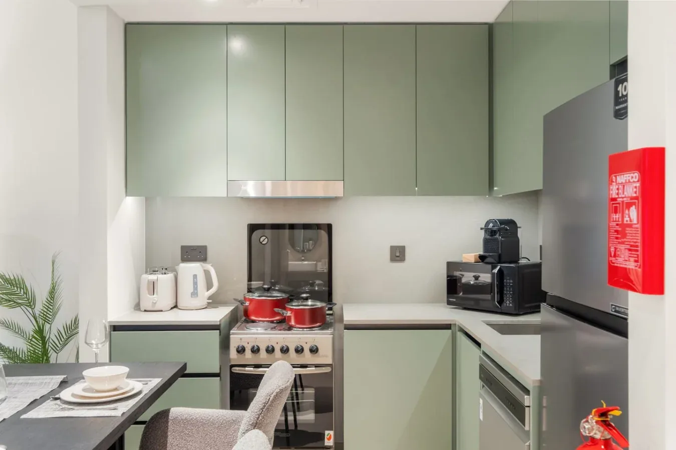 Una cocina compacta con gabinetes verdes, una estufa y electrodomésticos sobre la encimera.