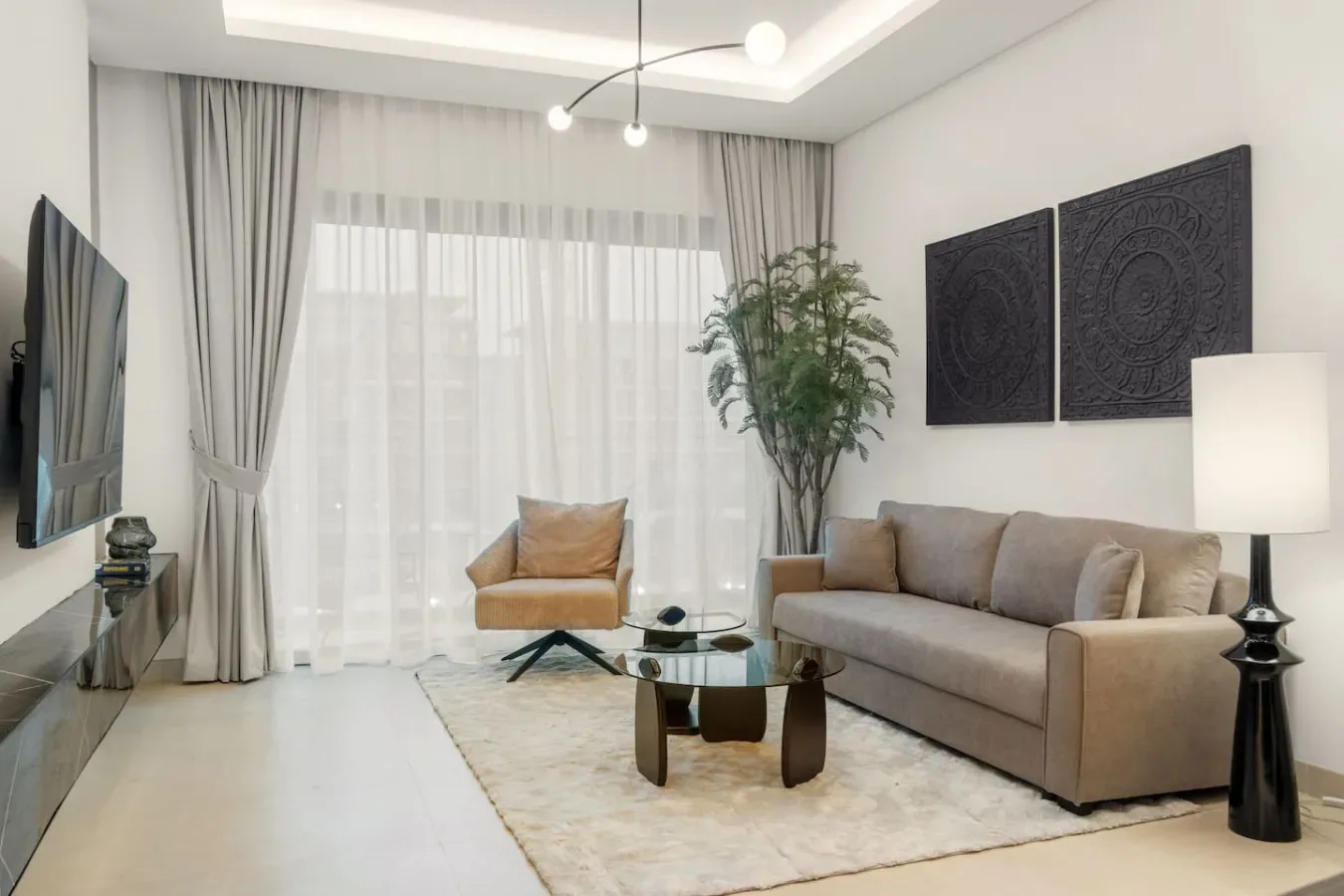 Una sala de estar luminosa con asientos, una mesa de centro de vidrio y grandes ventanas con cortinas.