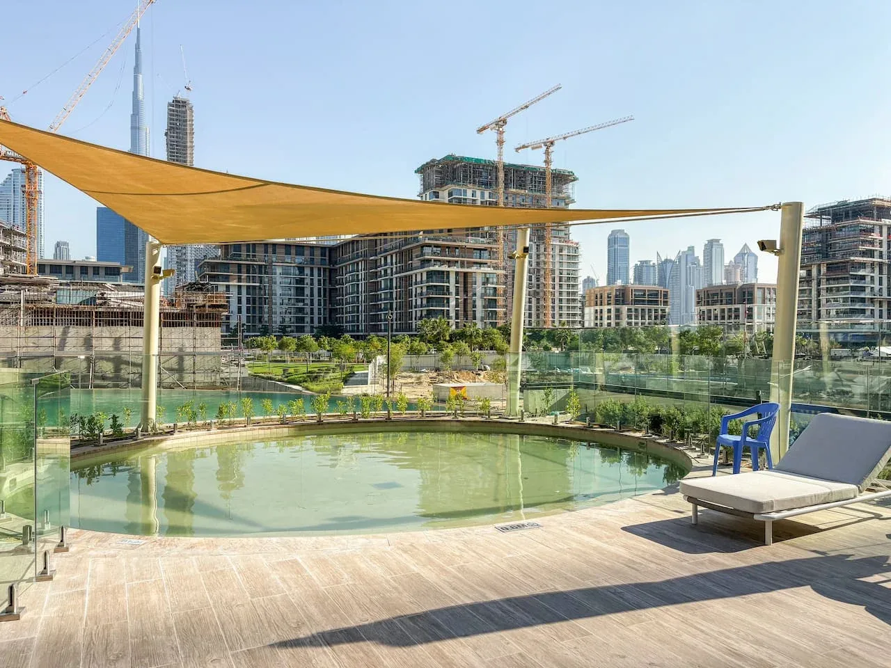 Una piscina al aire libre junto a una terraza de madera, asientos y una cubierta de sombra.