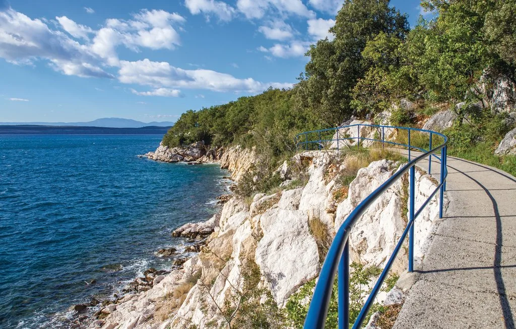 A curved coastal walkway follows a rocky shoreline beside blue water.