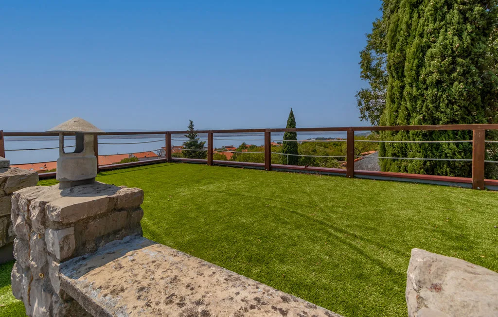 A grassy terrace with a stone bench and railing overlooks the surrounding landscape.