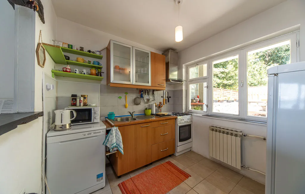 A compact kitchen with wooden cabinets, appliances, and a window overlooking greenery.