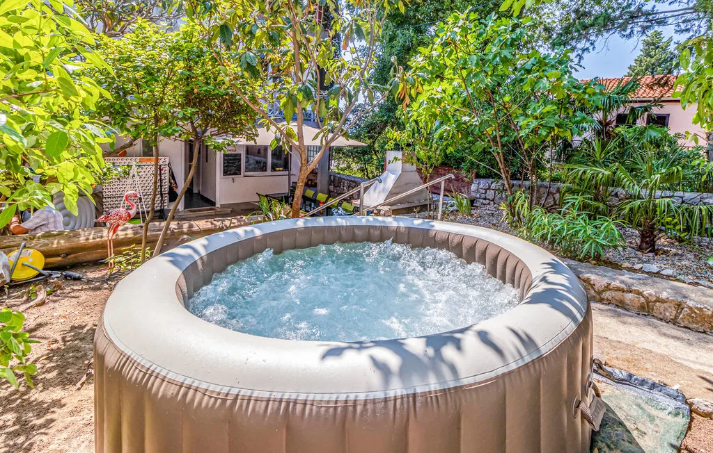 An outdoor hot tub sits in a leafy garden beside a house.
