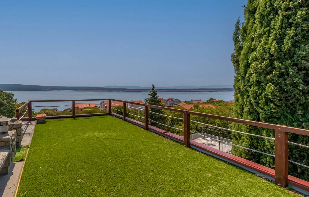 A grassy terrace with a railing overlooks a body of water.