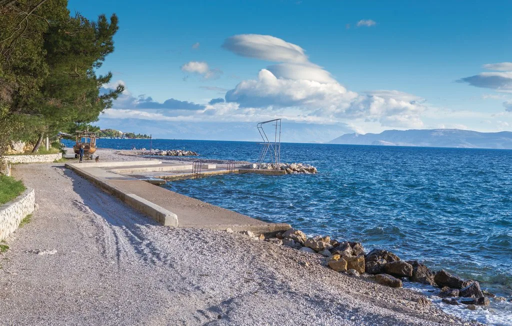 A pebble beach borders a blue sea, with a low concrete seawall along the shore.