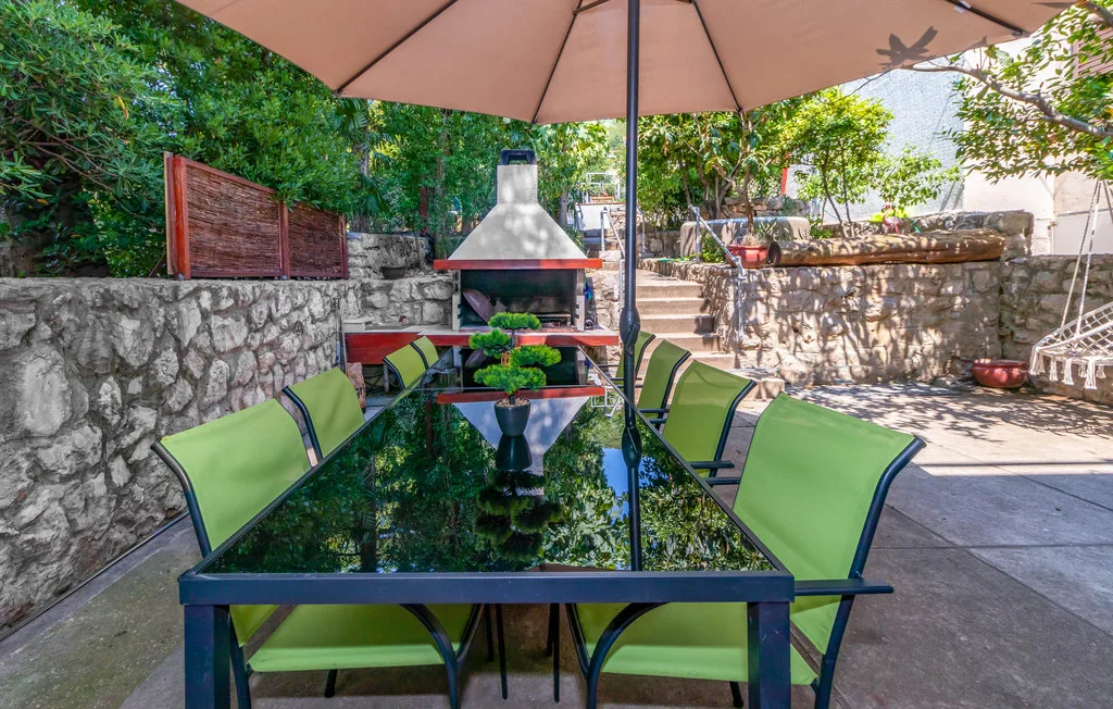 An outdoor dining area has a glass table and green seating beneath a large umbrella.