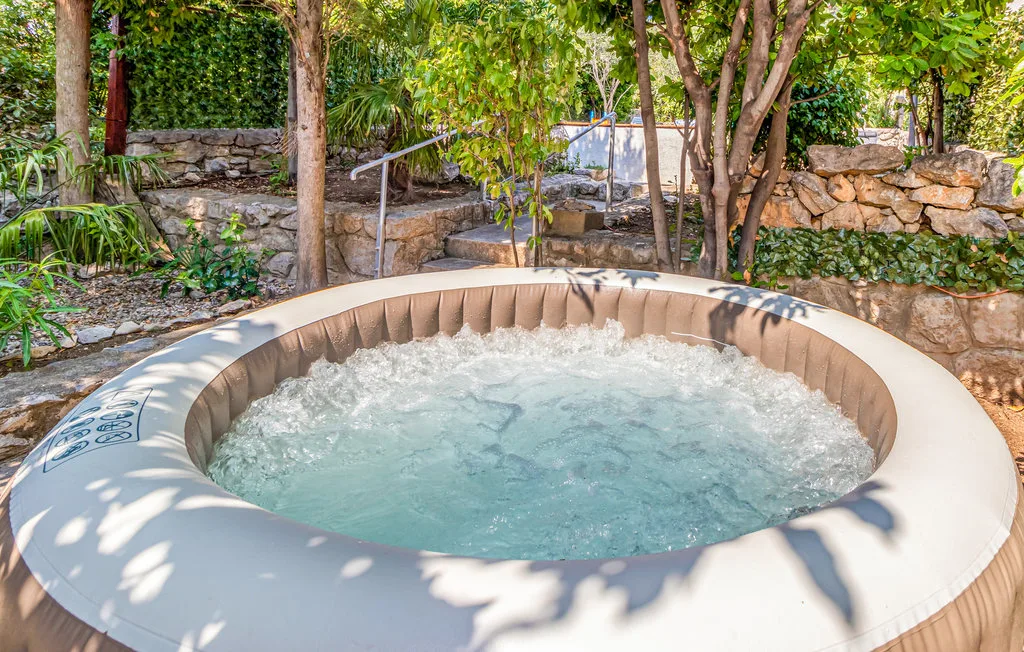 An outdoor hot tub bubbles among trees and stone garden walls.