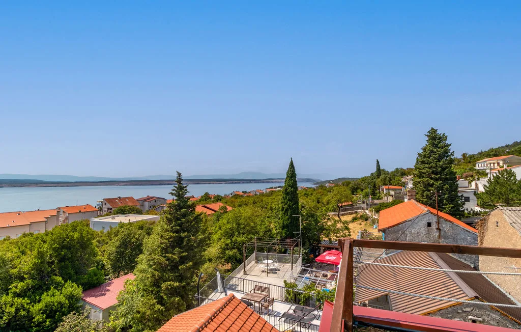 A coastal town with red-roofed buildings, trees, and the sea in the distance.