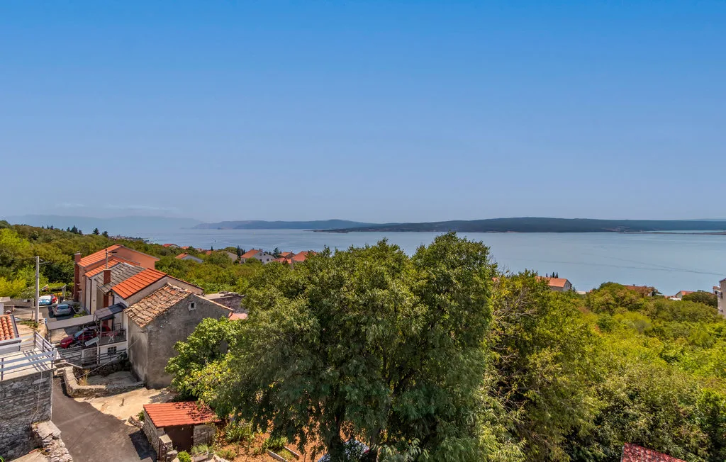A coastal landscape with red-roofed buildings, green trees, and water in the distance.
