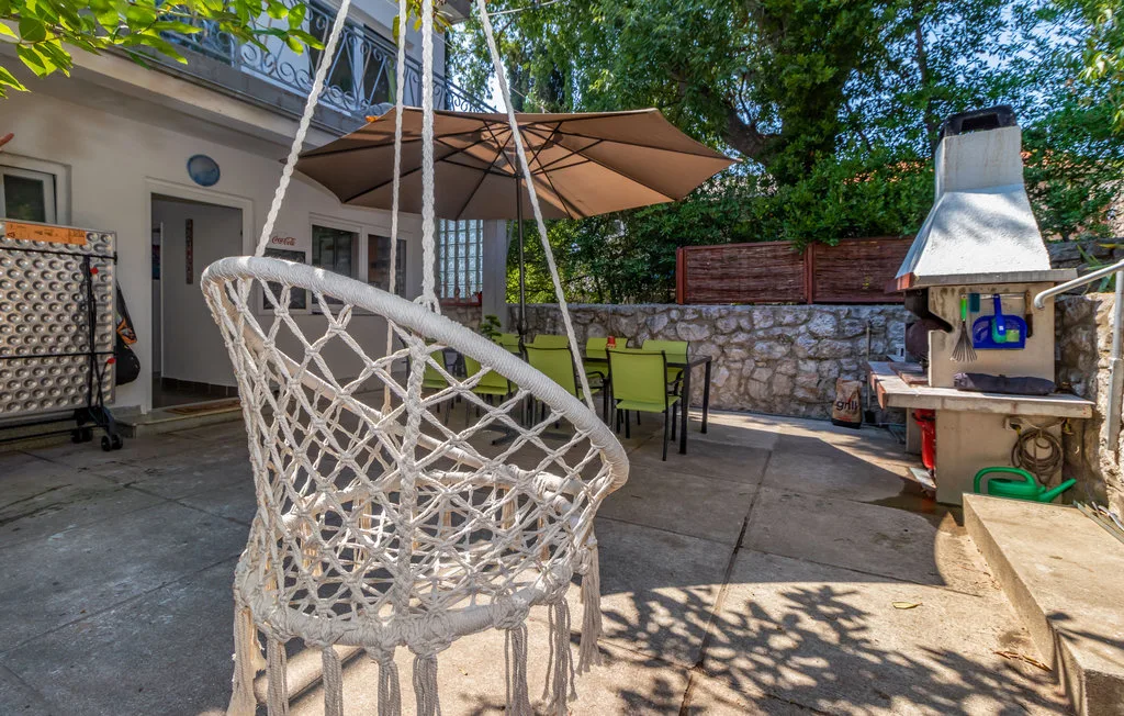 An outdoor patio has a hanging woven seat, shaded dining area, and stone barbecue.