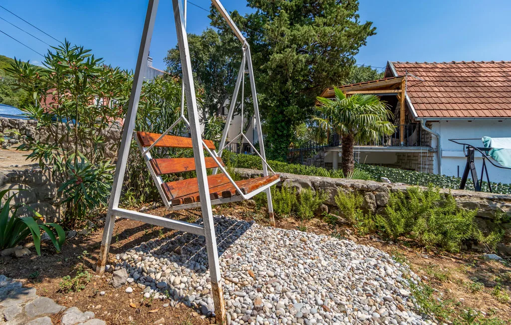 An outdoor garden seating area has a wooden swing above a bed of white stones.