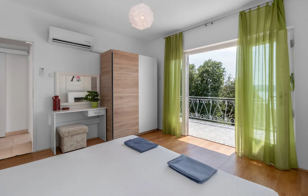 A bright bedroom with a desk and green curtains framing an open balcony doorway.