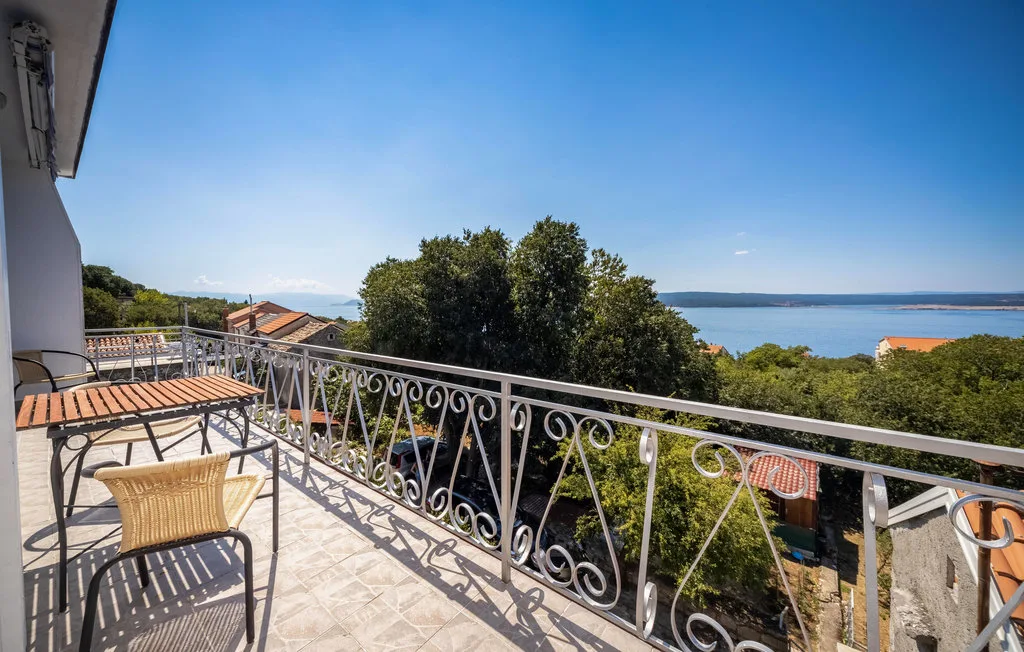 A tiled balcony with metal railings overlooks trees and a bay.