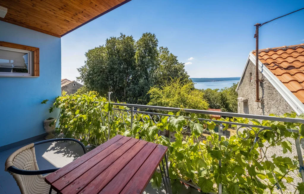 A balcony dining area overlooks leafy trees and a view of the sea.