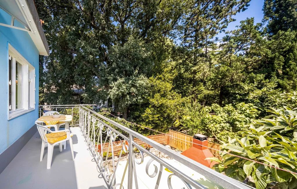 A balcony with white seating overlooks a leafy garden.