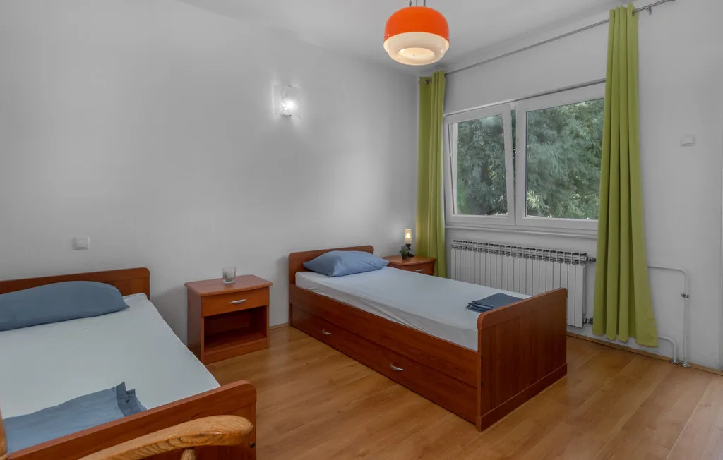 A bedroom with two beds, green curtains, and a large window.